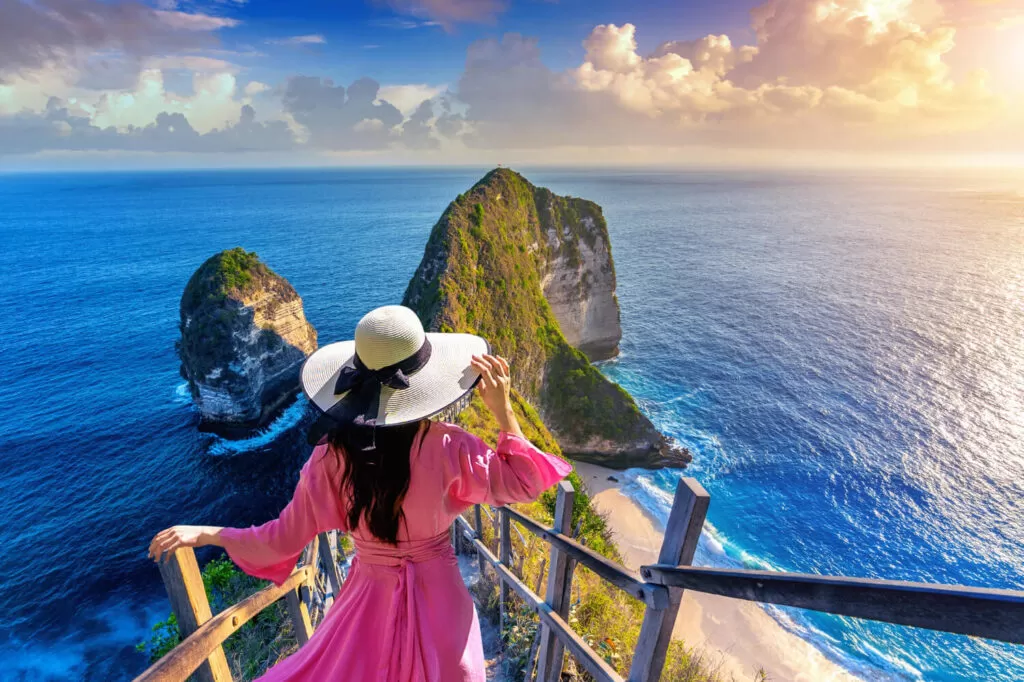 A girl in a pink dress with hat in front of Nusa penida beach in Bali